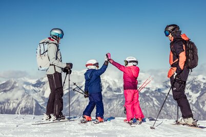 Eine Familie steht am Rand der Skipiste und genießt die schöne Aussicht auf die Winterlandschaft, die Kinder klatschen ein  | © Alpbachtal Tourismus | shootandstyle 