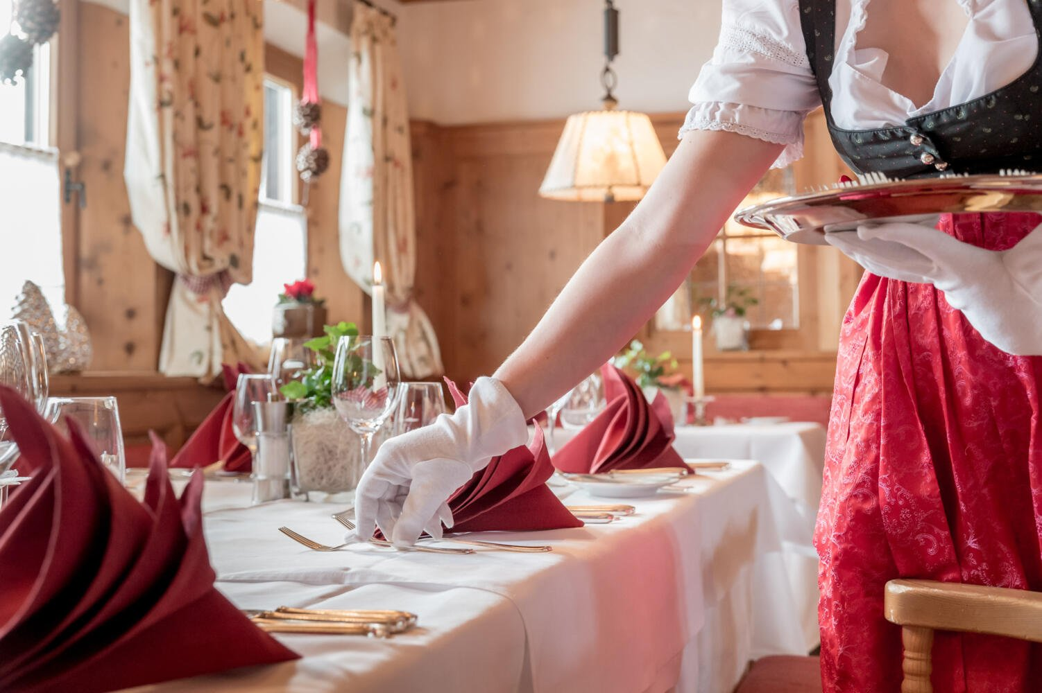 Auf diesem Bild ist eine Frau im Dirndl, mit weißen Handschuhen beim Tisch eindecken zu sehen  | © Hotel Böglerhof 