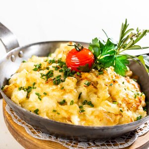 Eine Pfanne voller Käsespätzle, garniert mit Schnittlauch, einer gedämpften Tomate, Petersilie und ein bisschen Rosmarin  | © Stockerwirt Reith i.A. 