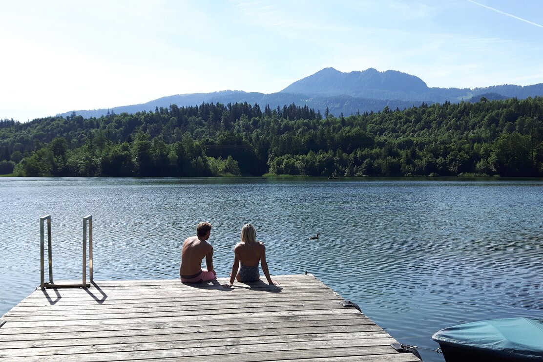 Auf diesem Bild sieht man wie ein Paar am Steg des Reintalersees sitzt und den Ausblick genießt  | © Alpbachtal Tourismus 