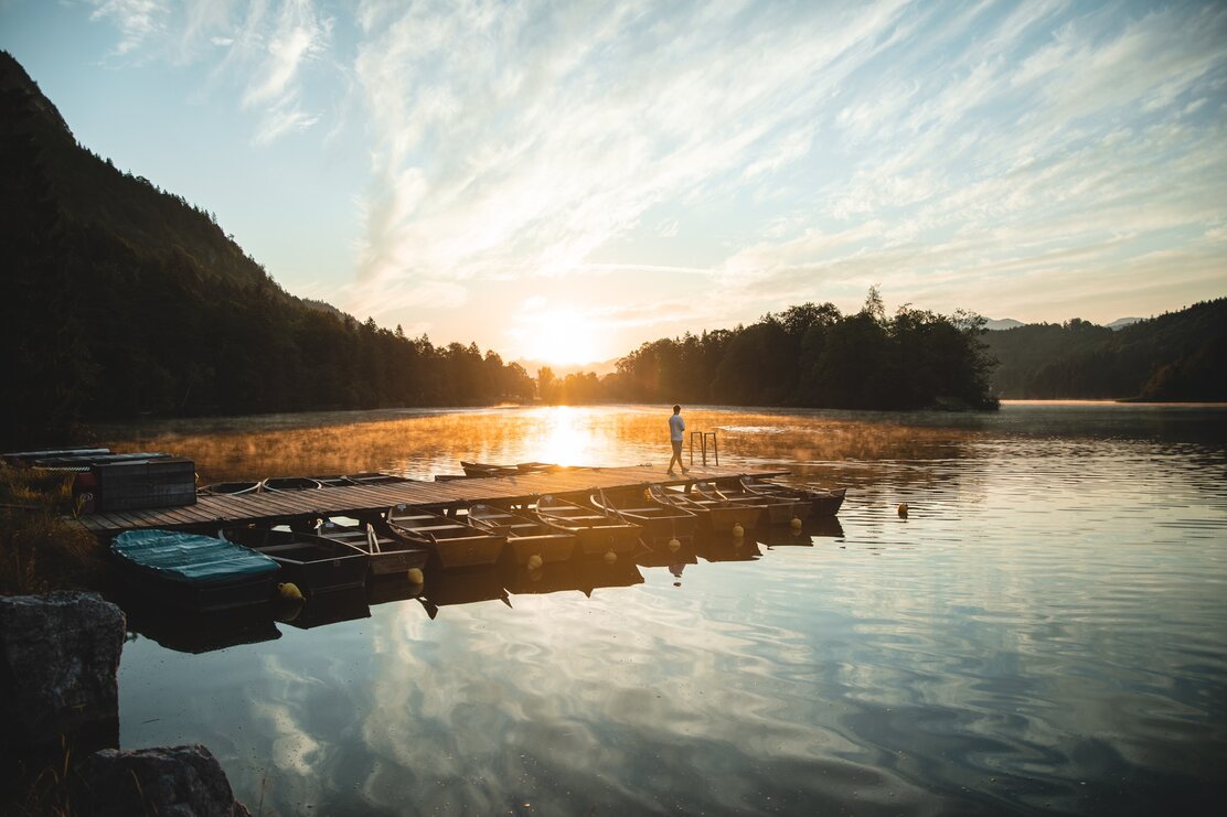 Ein Mann genießt am Steg des Reintalersees die ruhige Morgenstimmung mit Sonnenaufgang  | © TwoSomePionees | Maja Eifert 