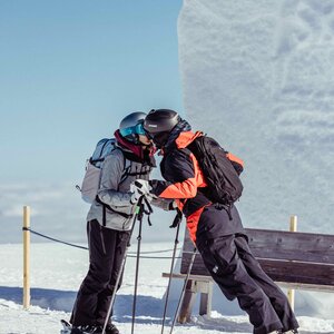 Auf diesem Bild zu sehen ist eine Frau und ein Mann, welche sich gerade auf der Piste küssen, im Hintergrund ein Fotospot mit einem Schneeherzen | © Alpbachtal Tourismus  | shootandstyle 