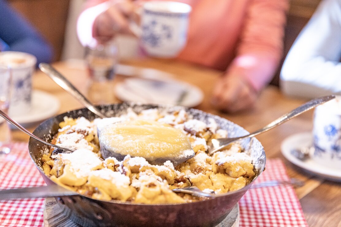 Auf diesem Bild sieht man eine Pfanne voller Kaiserschmarrn, in der Mitte eine Portion Apfelmus und rechts und links ragen einige Gabeln aus der Pfanne  | © Ski Juwel Alpbachtal Wildschönau | shootandstyle 